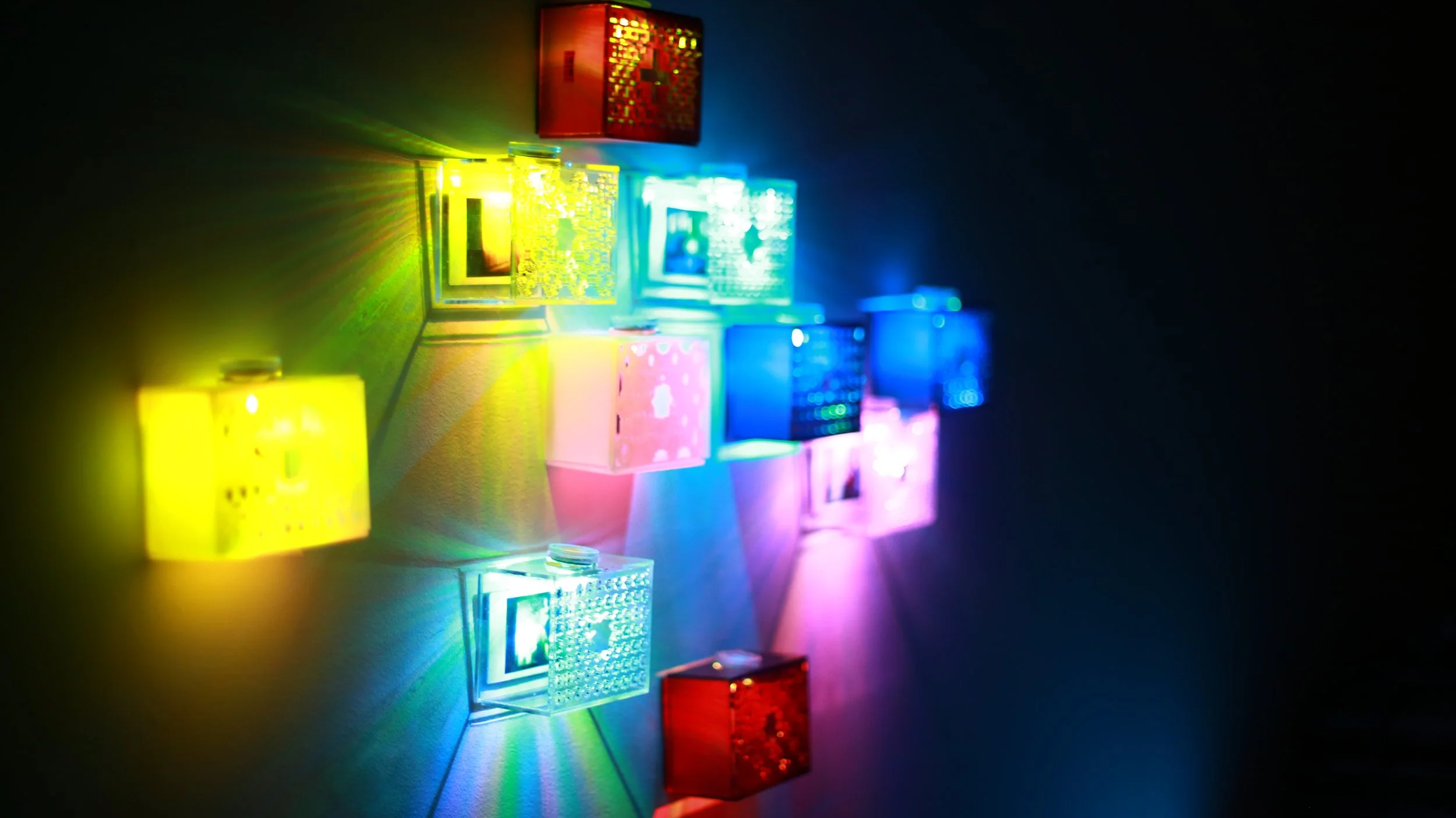 Colorful LED light blocks arranged on a wall, emitting red, yellow, blue, pink, and green lights, creating a vibrant light display with shadows on a dark background.