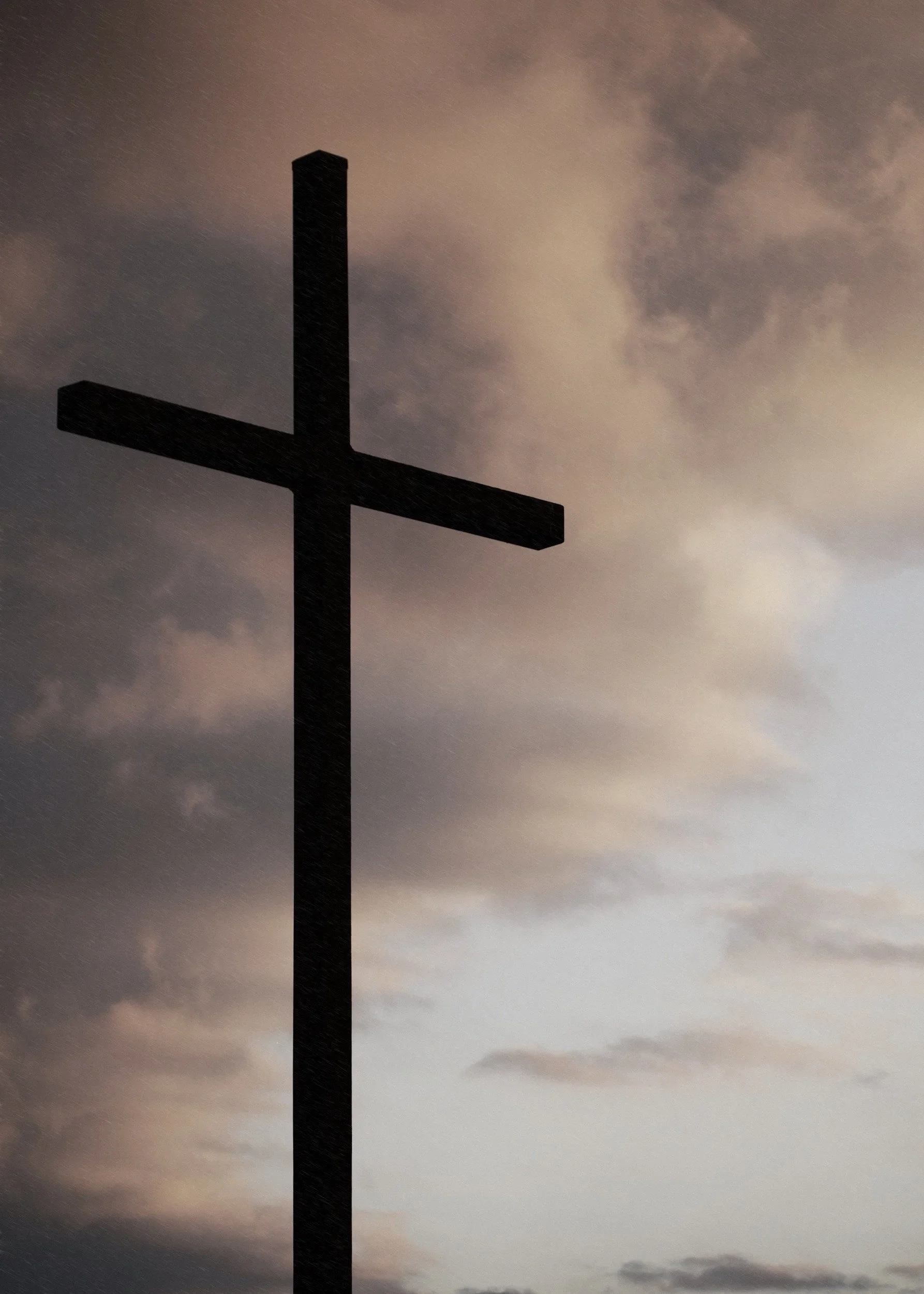 Silhouette of a tall cross against a cloudy sky at dusk or dawn.