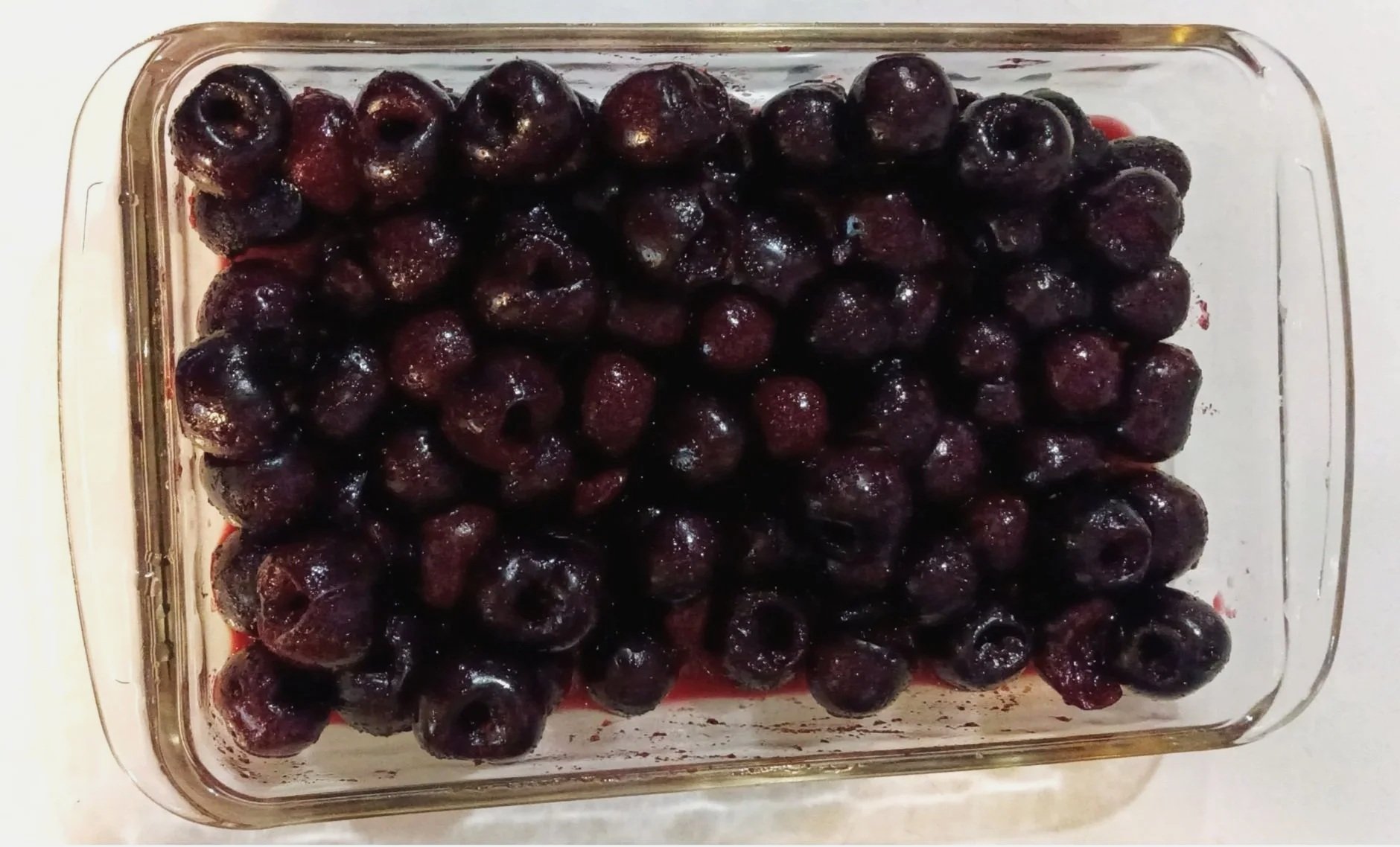 Pitted dark sweet cherries in a rectangular Pyrex baking dish, ready for Honey Sweet Cherry Cobbler.