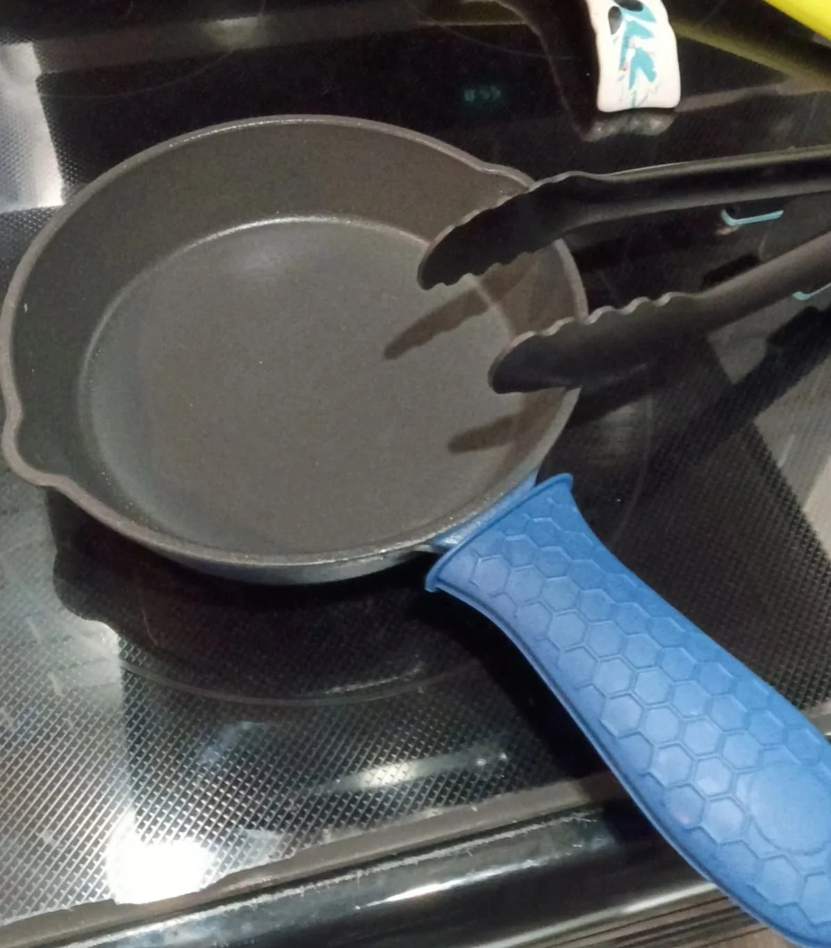 Zakarian by DASH 7.5-inch nonstick cast iron skillet on a glass stovetop with a blue silicone handle cover added by the owner. The silicone handle cover is not included with the skillet.