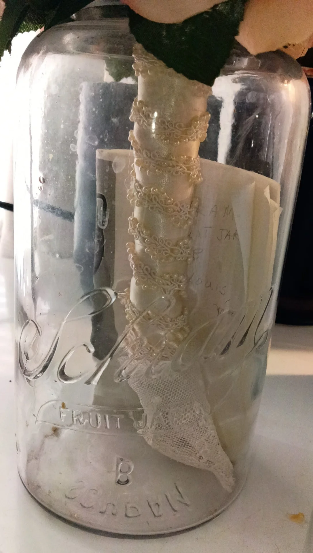 Clear half-gallon Schram fruit jar holding a preserved wedding bouquet, with the embossed Schram Fruit Jar lettering visible on the glass.