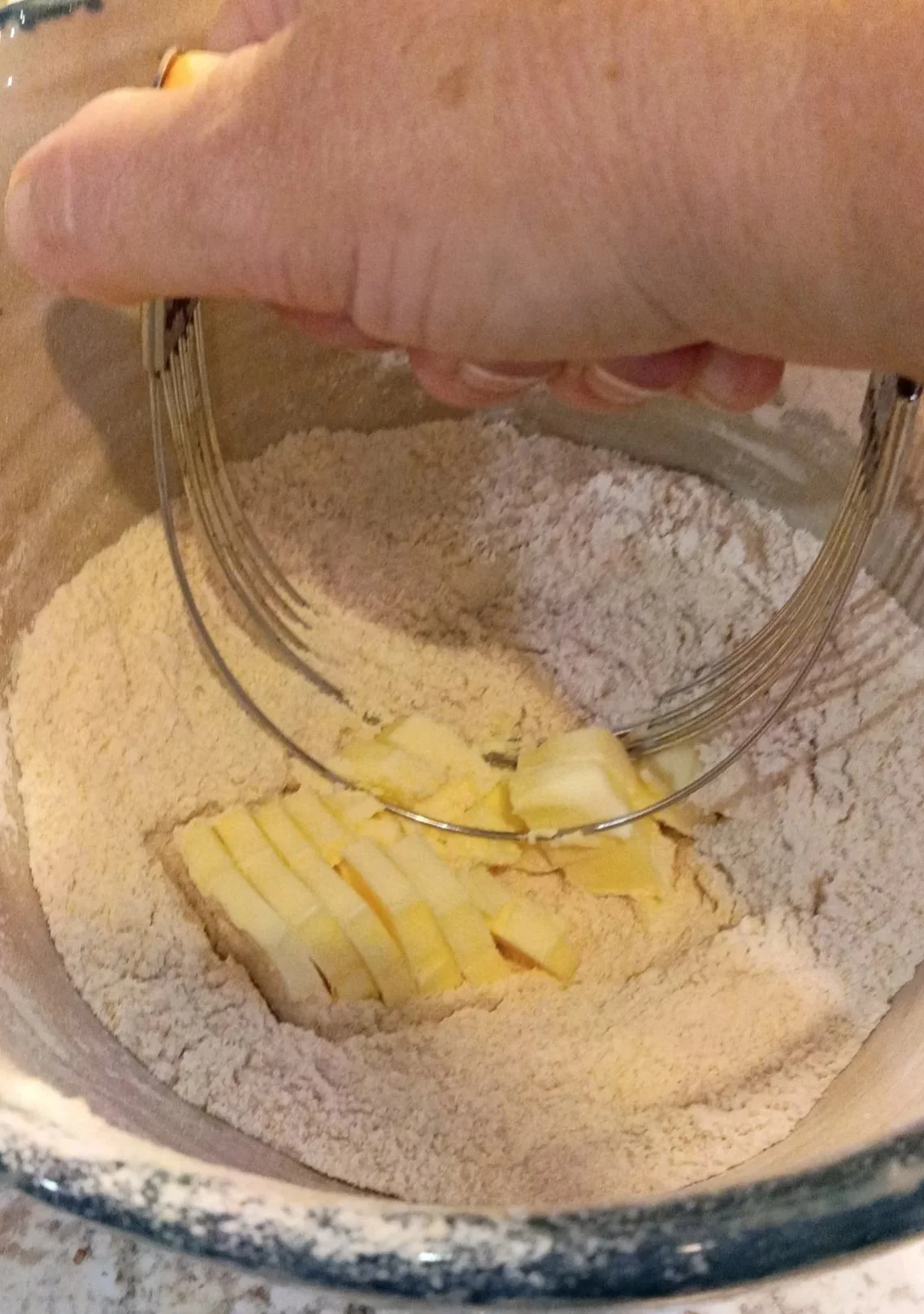 Cold butter being cut into fresh milled flour with a pastry blender for the cobbler topping.