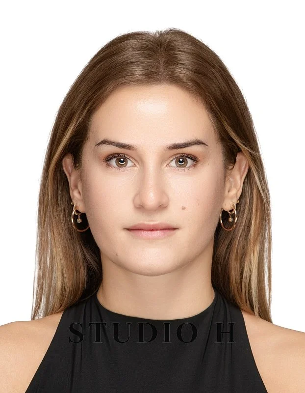 Close-up portrait of a young woman with light brown hair, wearing hoop earrings and a black sleeveless top, facing forward with a neutral expression.