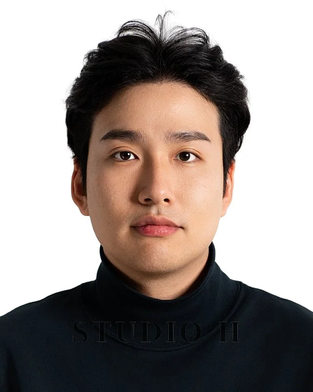 Portrait of a young man with black hair wearing a black turtleneck shirt against a plain white background.