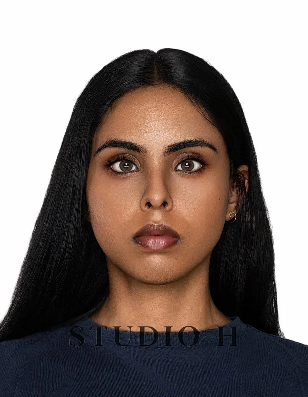 Portrait of a young woman with long black hair, wearing a dark blue top, with a neutral expression, set against a plain white background.