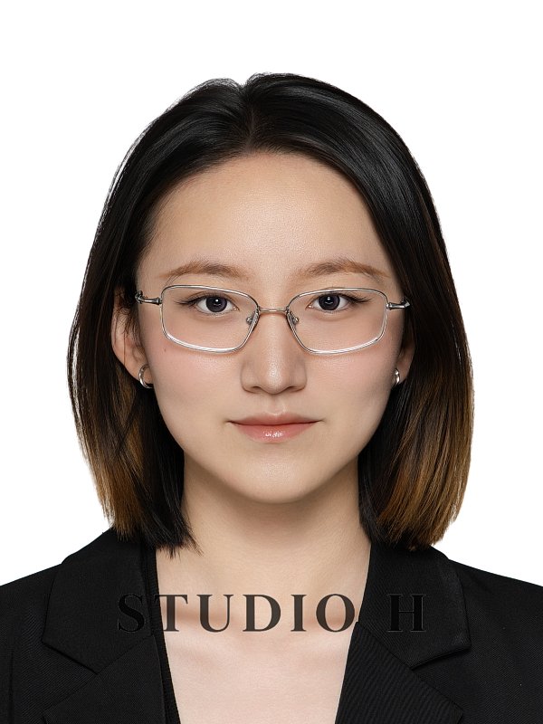 A young woman with shoulder-length dark hair, wearing glasses, silver earrings, and a black blazer, looking directly at the camera against a white background.
