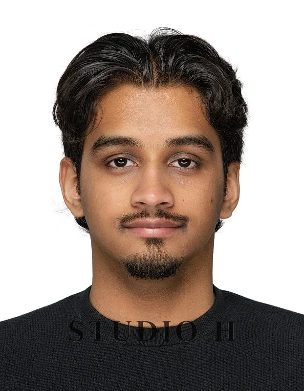 Portrait of a young man with dark hair and a goatee, wearing a black shirt, against a white background.