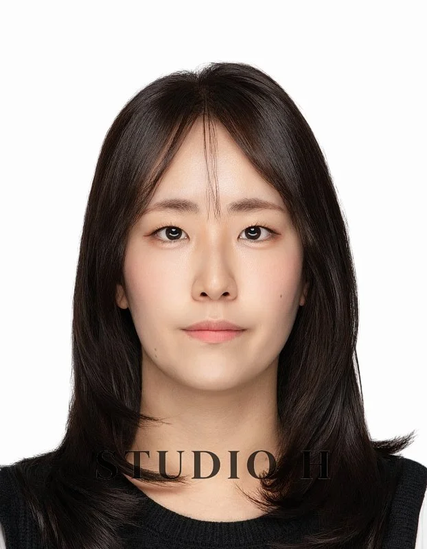 Portrait of a young woman with straight, shoulder-length dark hair, wearing a black top, against a plain white background.