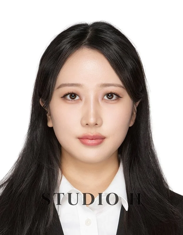 A woman with long black hair wearing a white shirt and black jacket, looking directly at the camera against a white background.
