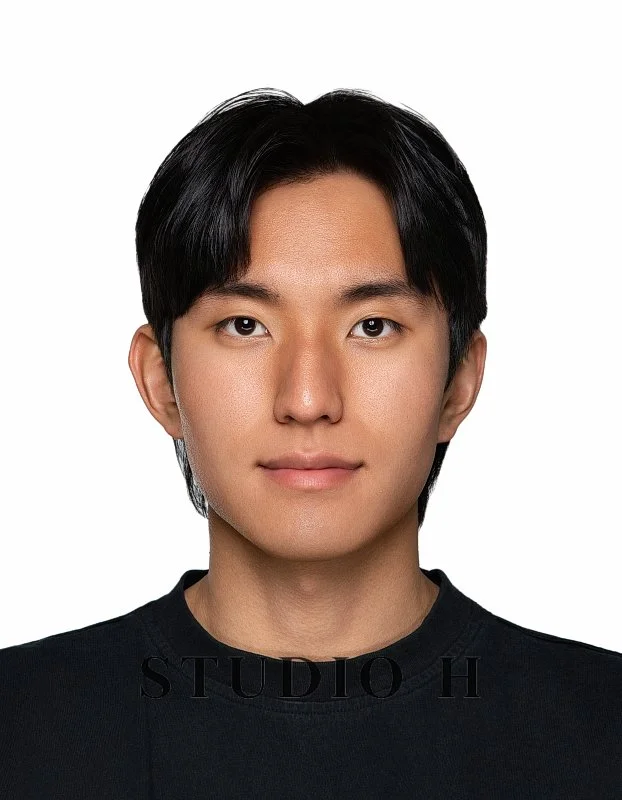 Portrait of a young Asian man with black hair, wearing a black shirt, smiling slightly against a plain white background.