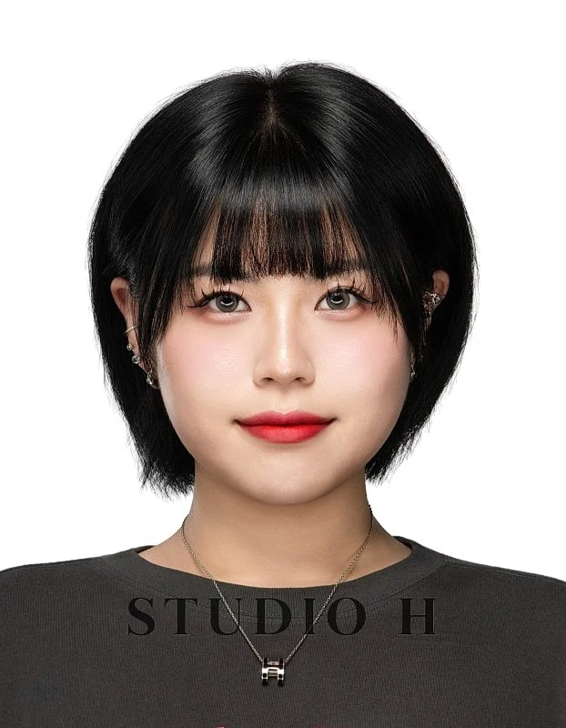 Portrait of a young woman with short black hair and bangs, wearing earrings and a necklace, with a subtle smile, against a white background and the text 'STUDIO H' at the bottom.