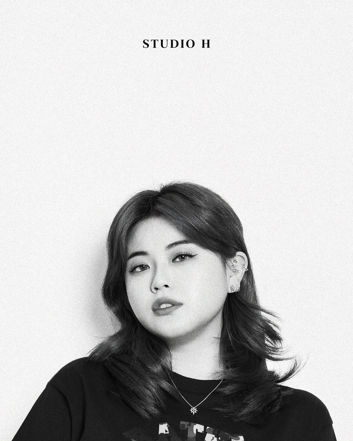 Black and white portrait of a woman with shoulder-length hair, looking at the camera, wearing earrings and a necklace, with the text 'STUDIO H' at the top.