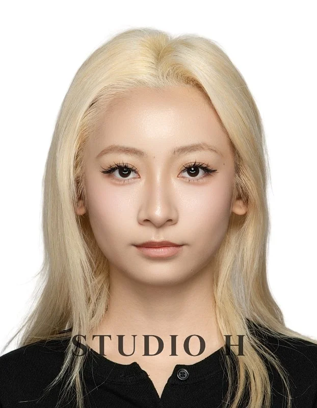 A portrait of a young woman with platinum blonde hair, light makeup, and a black top, against a white background.