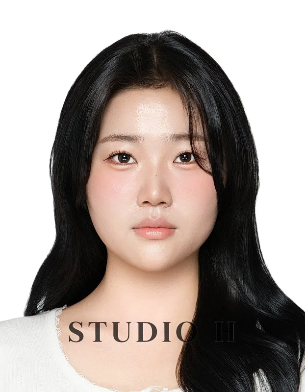A portrait of a young woman with long black hair, light skin, and subtle makeup, against a plain white background.