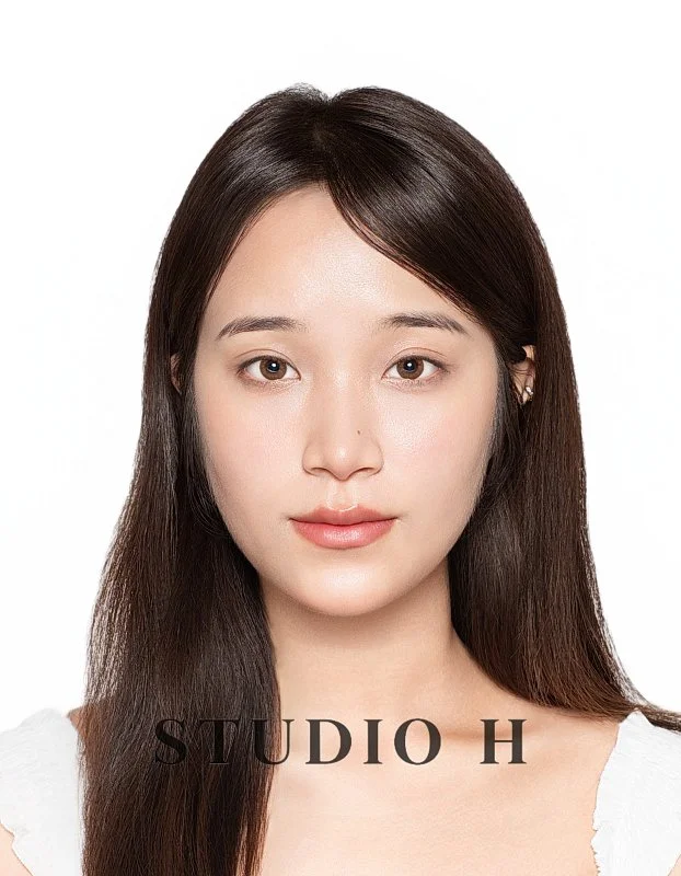 A portrait of a young woman with straight brown hair and light skin, wearing a white top, against a plain white background, with the text 'STUDIO H' at the bottom.