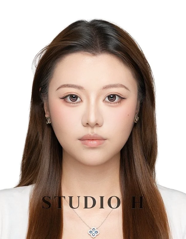 Portrait of a young woman with long brown hair, wearing makeup, earrings, and a necklace, against a white background with the text 'STUDIO H' at the bottom.