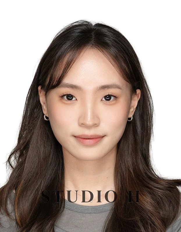 A young woman with long brown hair, wearing small hoop earrings and a gray top, smiling slightly against a white background. Text at the bottom reads 'STUDIO H'.