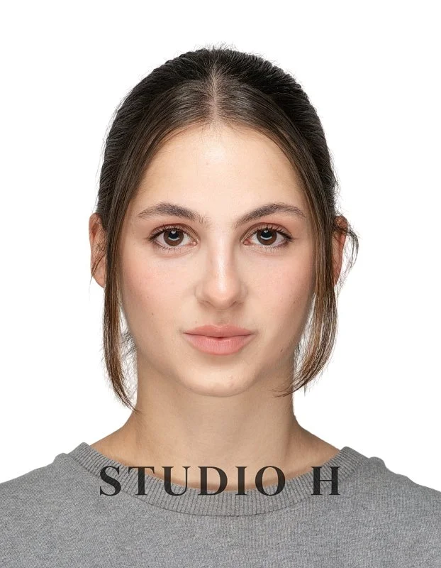 Headshot of a young woman with brown hair in a simple gray top, facing the camera with a neutral expression, against a plain white background with the text 'STUDIO H' at the bottom.