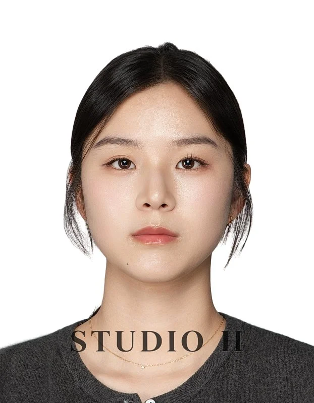 A close-up portrait of a young Asian woman with black hair, wearing a dark top and a delicate necklace against a white background, with the text 'STUDIO H' at the bottom.