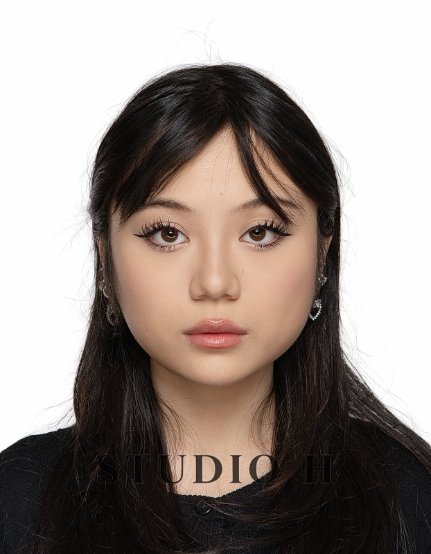 Portrait of a young woman with long dark hair, wearing earrings, and a black top, against a plain white background.