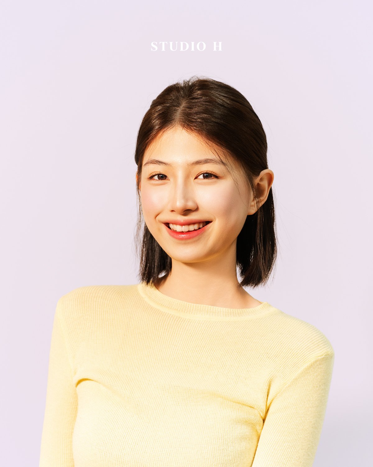 Young woman with short dark hair wearing a light yellow top smiling at the camera. Text above her head reads 'STUDIO H'.