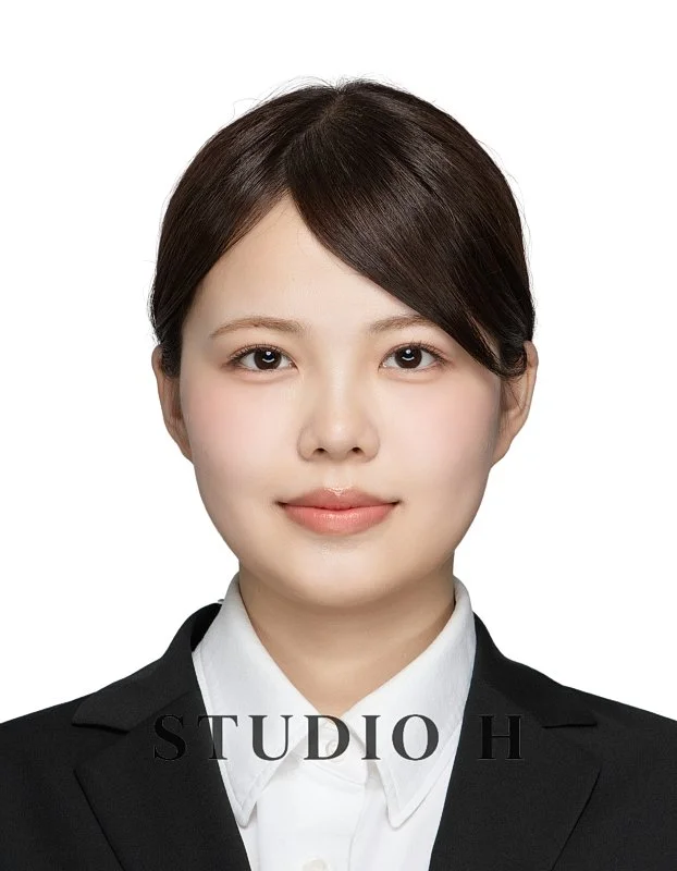 Portrait of a young woman with short brown hair, wearing a black blazer and white shirt, smiling softly against a white background.