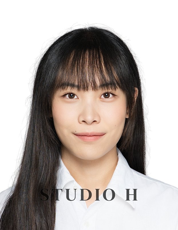 A young woman with long black hair and bangs, wearing a white collared shirt, smiling softly at the camera against a plain white background.