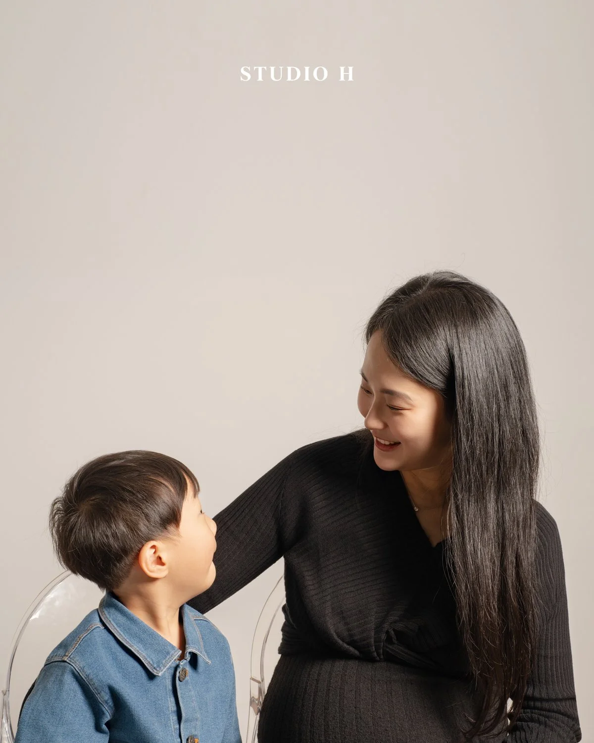 A woman and a young boy facing each other and smiling, sitting against a plain beige background with the text 'STUDIO H' at the top.