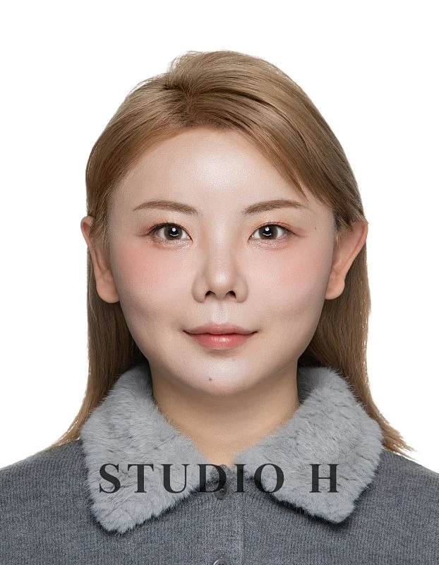 Portrait of a woman with light brown hair wearing a gray coat with a faux fur collar, against a white background, with text "STUDIO H" at the bottom.