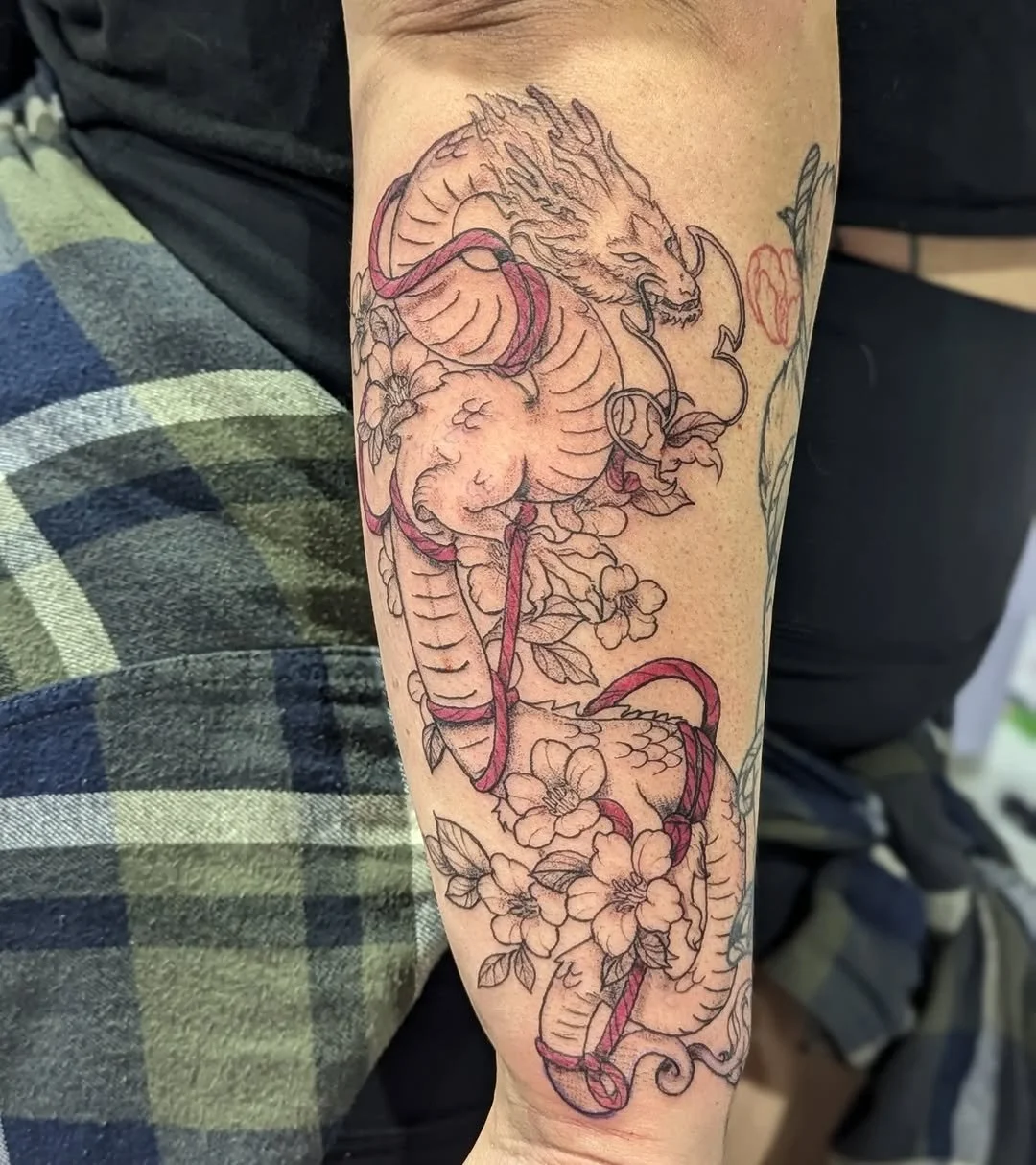 Tattoo of a dragon intertwined with floral designs on an arm.