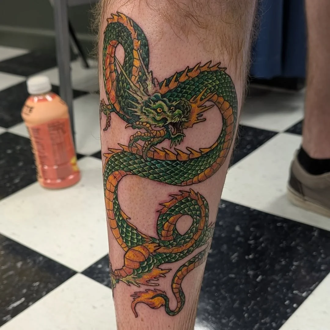 Tattoo of a green and orange Chinese dragon on a person's leg, coiled and fierce.