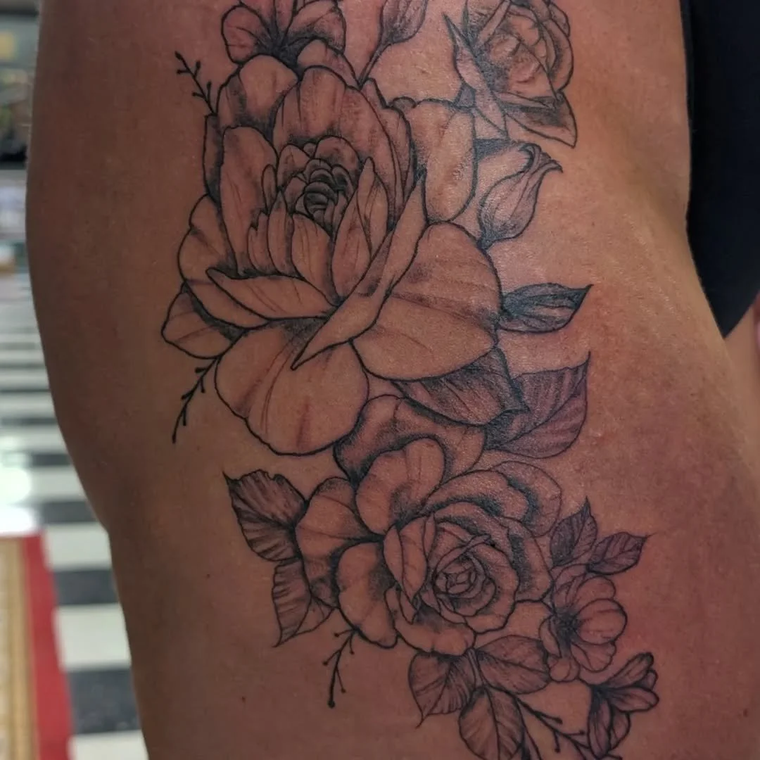Black outline floral tattoo of roses with leaves on skin.