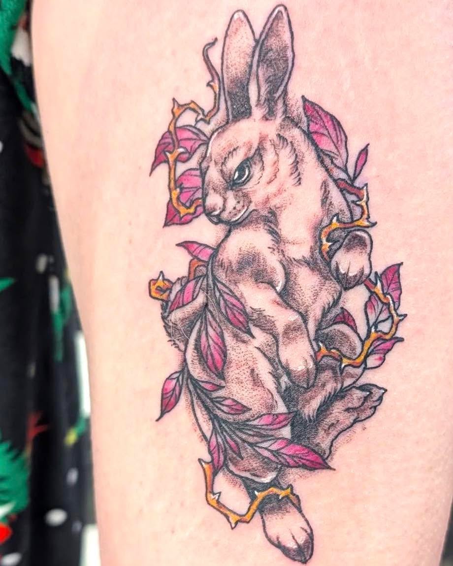 Tattoo of a realistic hare surrounded by pink leaves and yellow thorny vines.