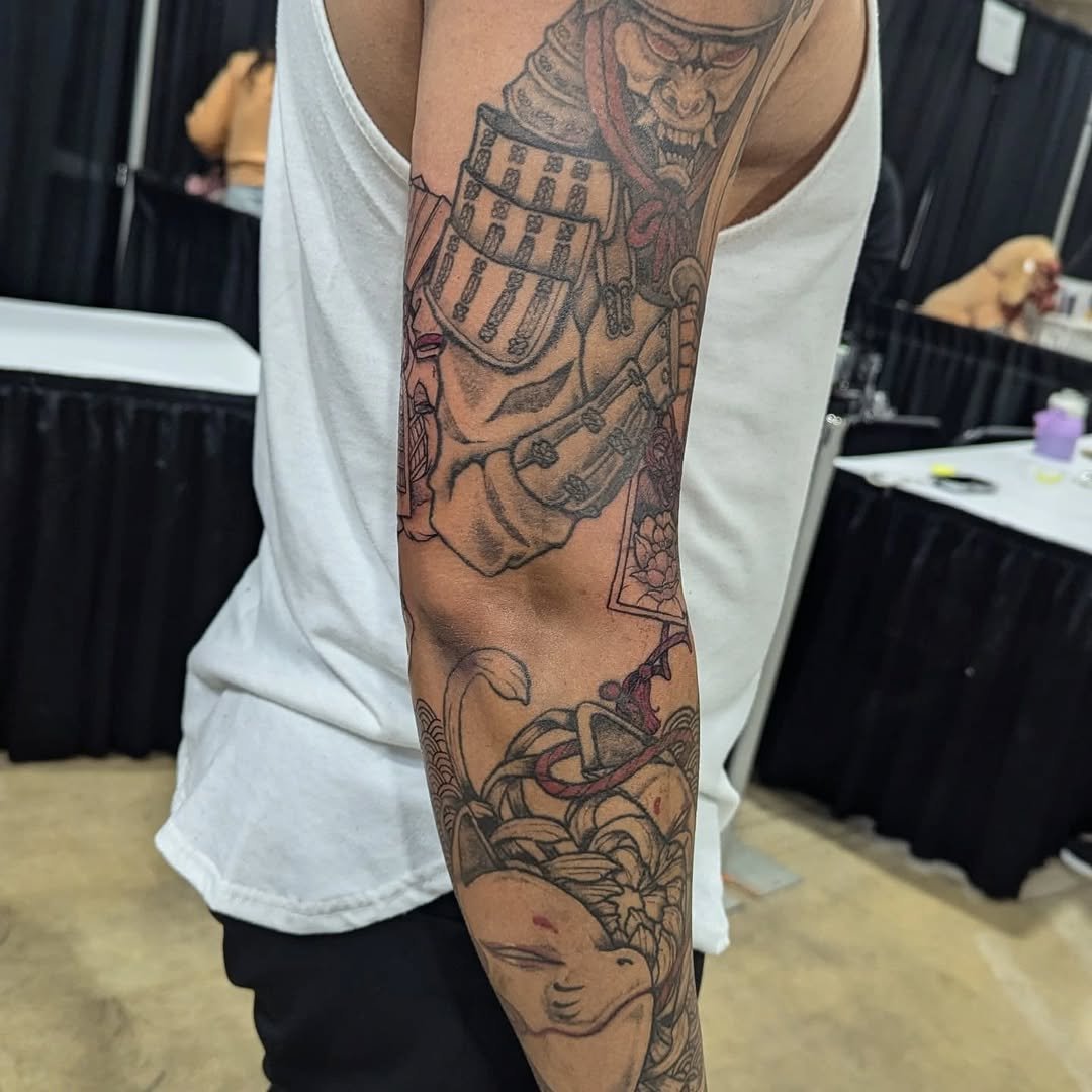 Tattoo of a Japanese warrior in armor holding a sword, with a dragon and floral designs on an arm.