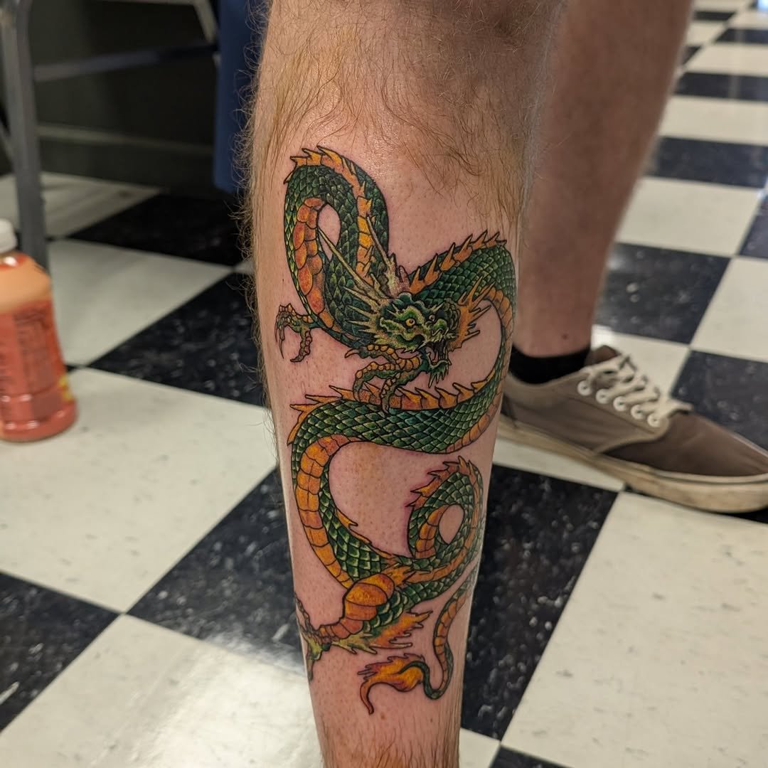 Colorful tattoo of a Chinese dragon on a person's lower leg, featuring green, orange, and yellow scales.