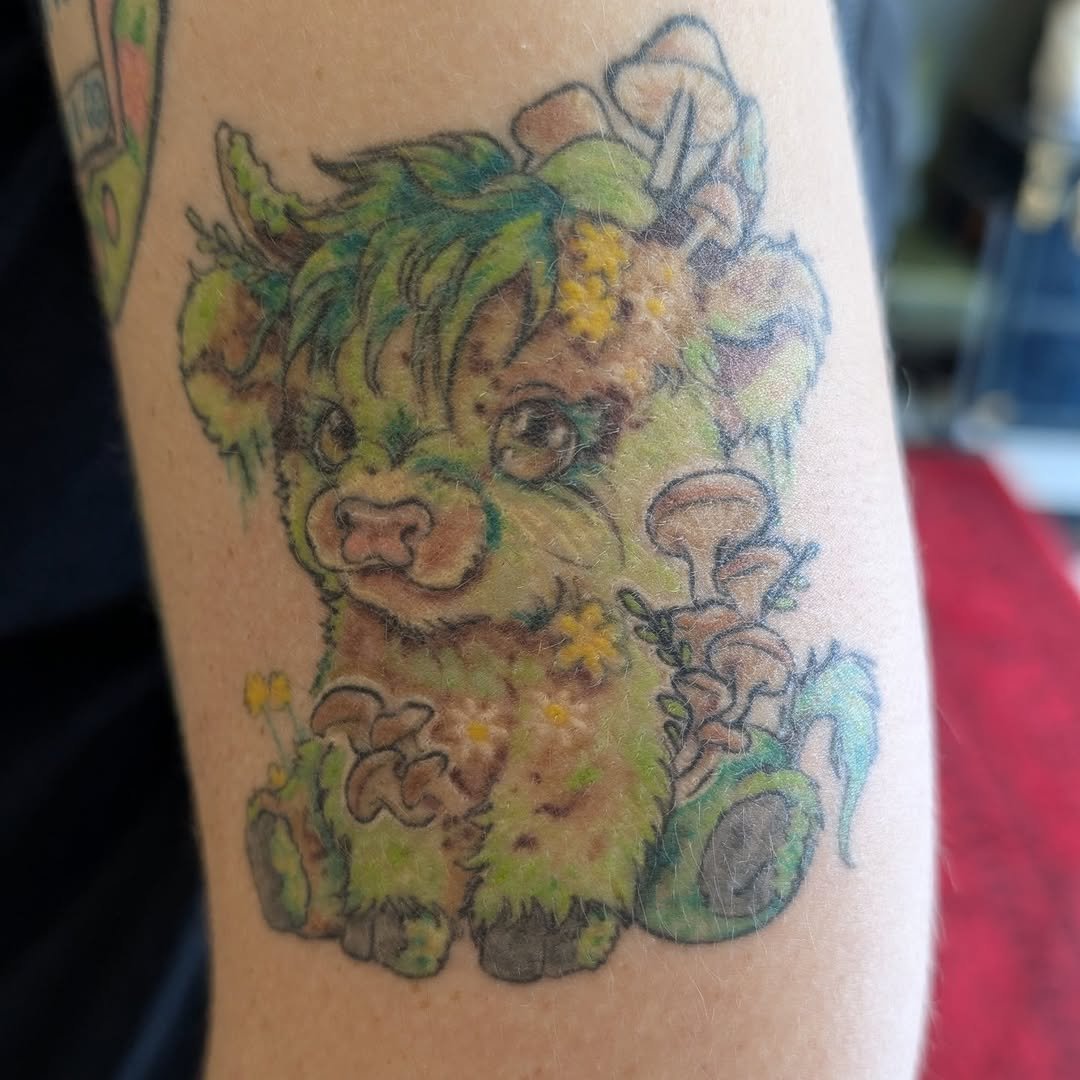 Colorful tattoo of a cute puppy with green and yellow fur, surrounded by flowers and mushrooms.