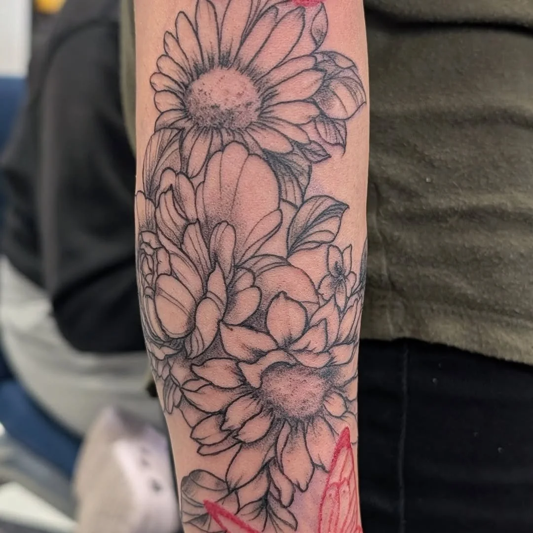 Black outline floral tattoo of daisies with shading on a person's arm.