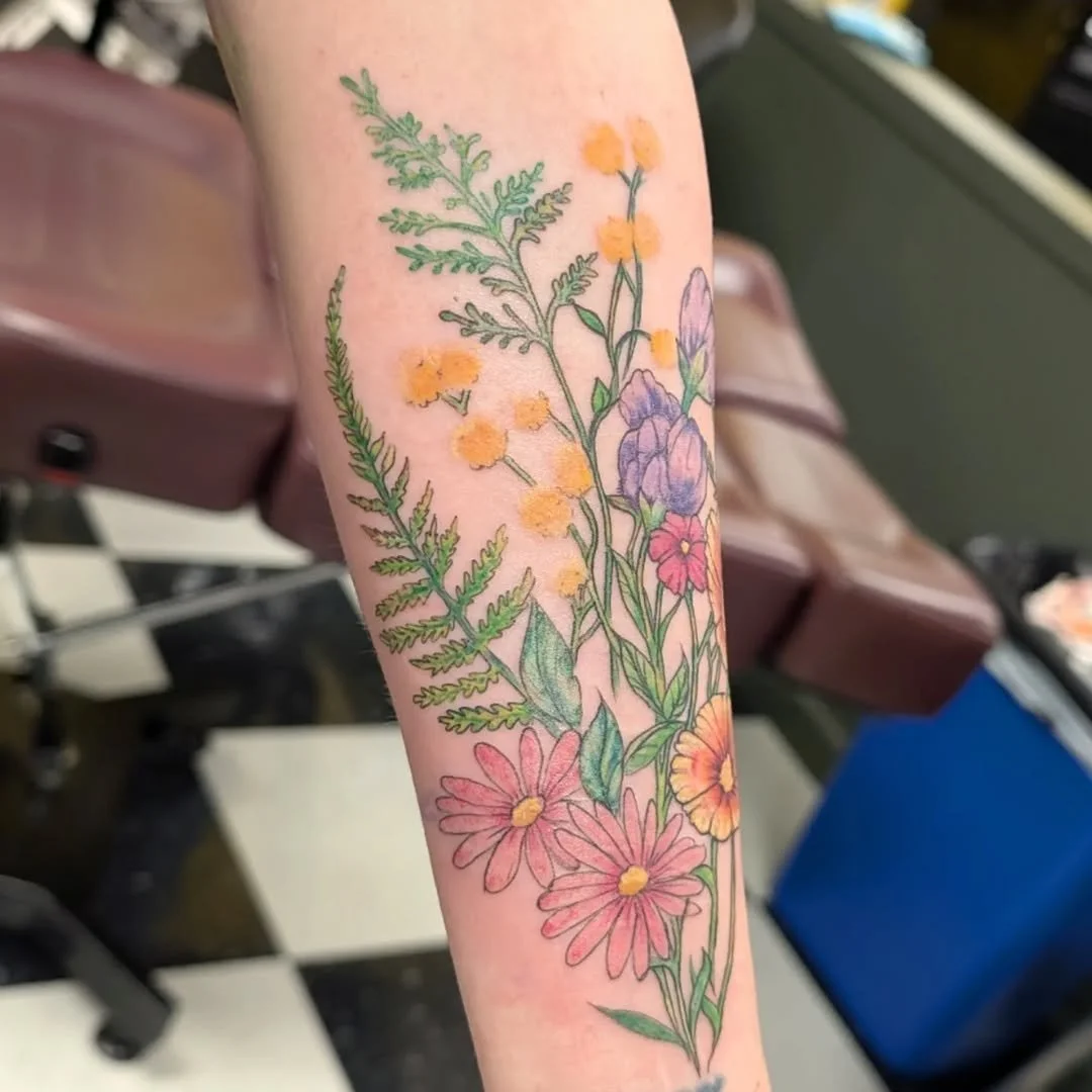Colorful floral tattoo on a person's arm with various flowers and green leaves.