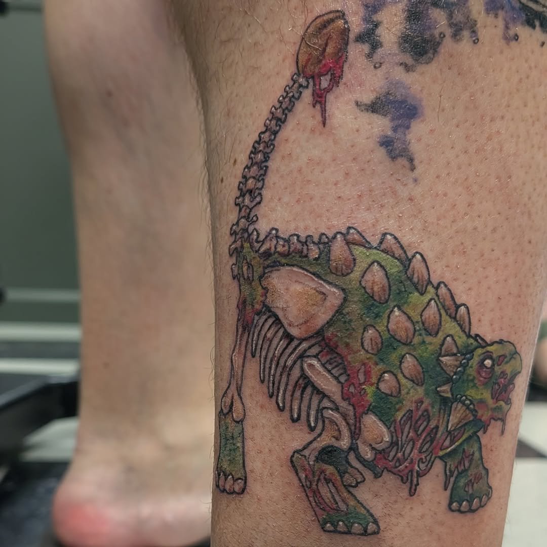 A colorful tattoo of a dinosaur, specifically a Triceratops, on a person's leg.