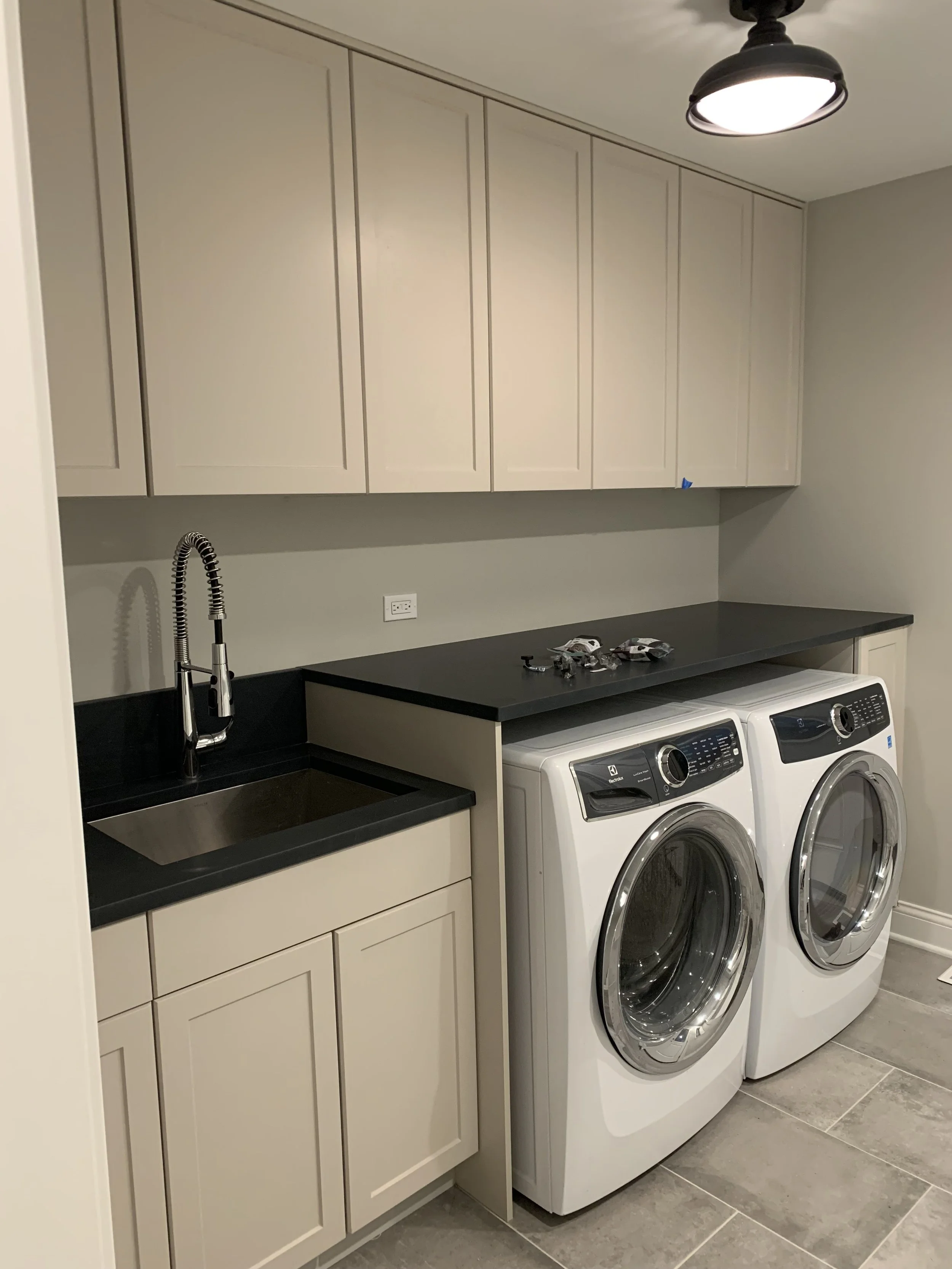 A laundry room with beige cabinets above a black countertop, a small sink with a black faucet, and a washing machine and dryer side by side. There are some small items on the countertop.