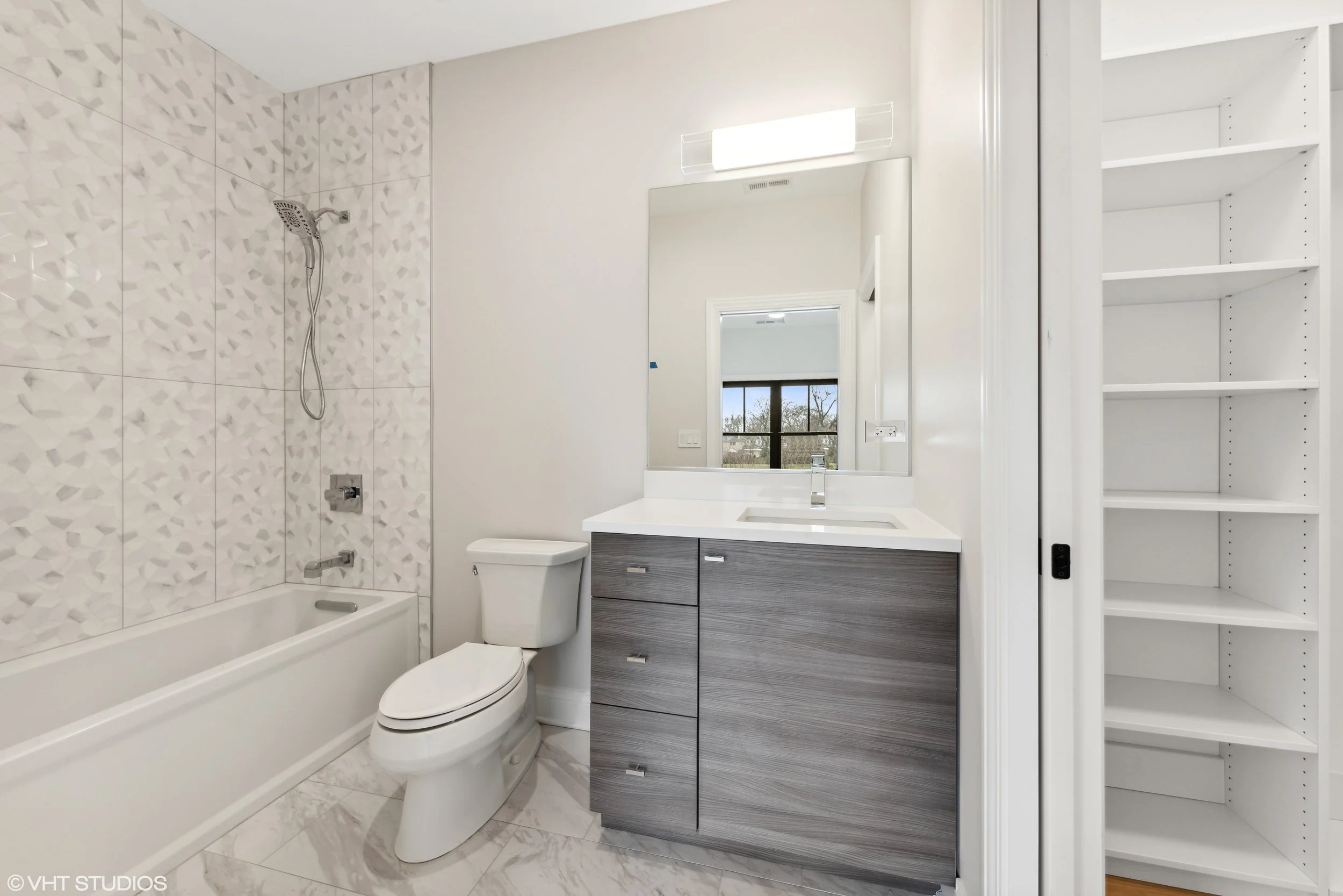 Modern bathroom with a shower/bathtub, toilet, vanity with a sink and mirror, and a closet with shelves.