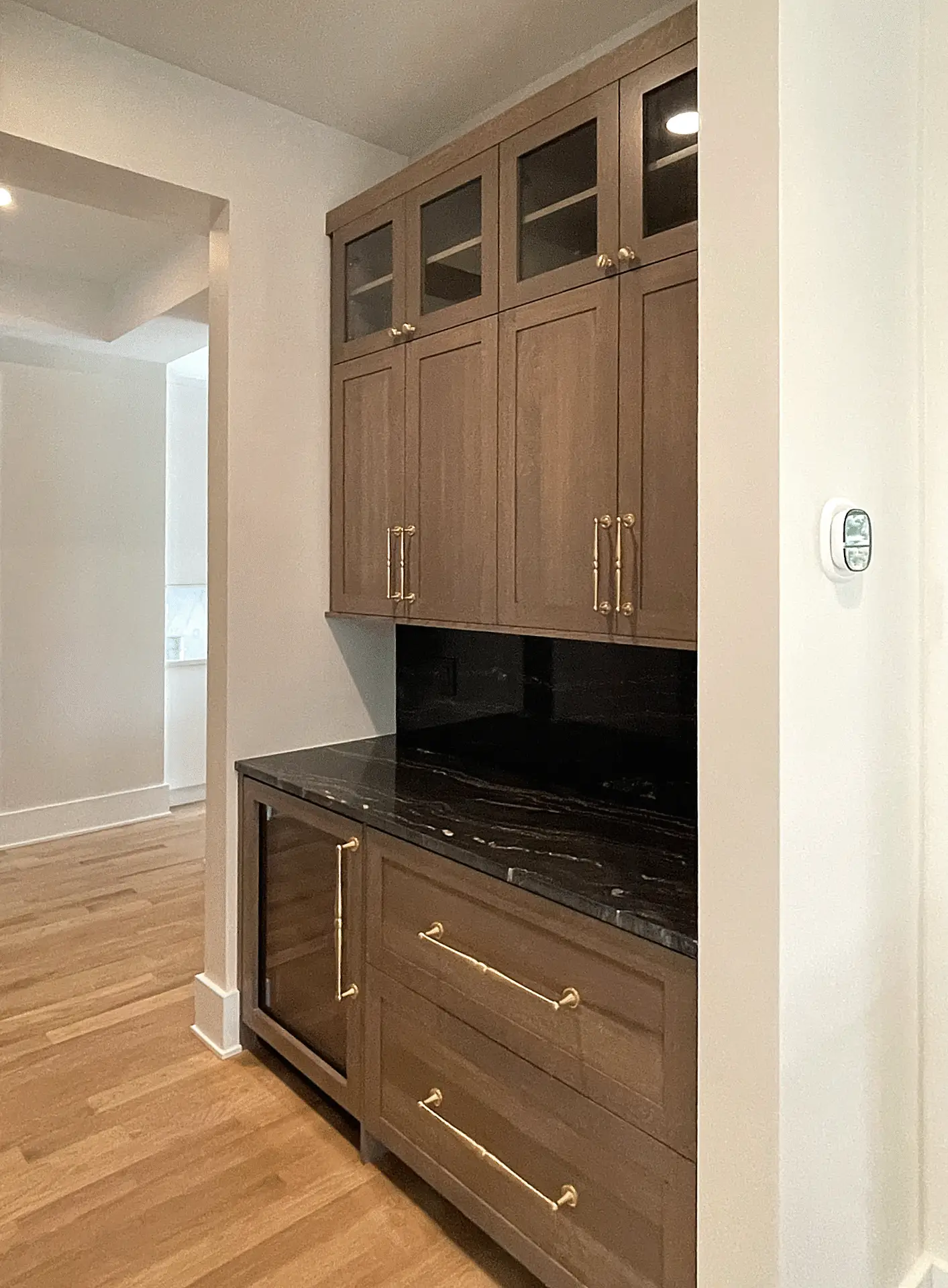 A built-in kitchen cabinet with wooden doors, brass handles, and black marble countertop, located against a white wall.