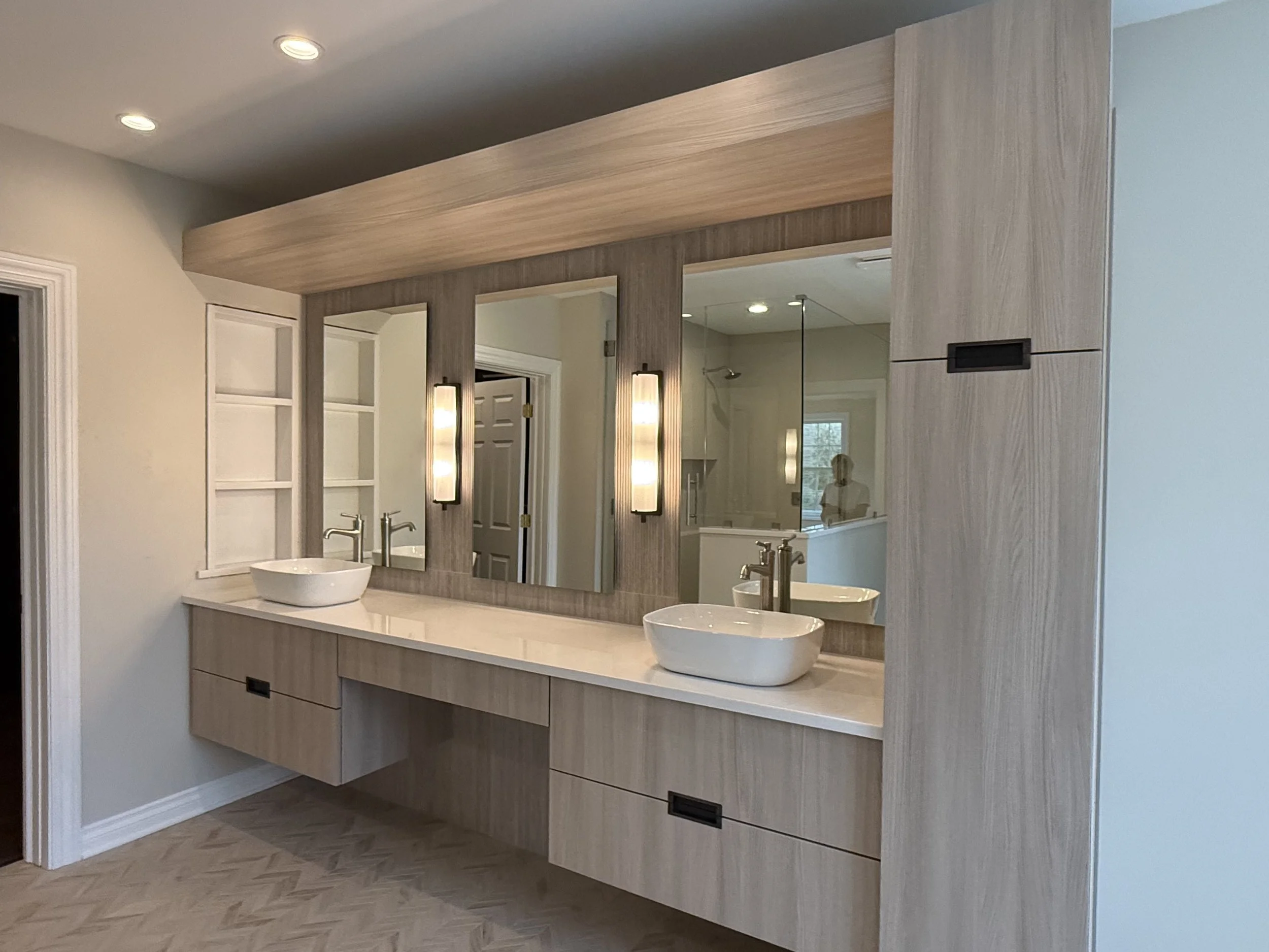 Modern bathroom vanity with two vessel sinks, large mirror, wall-mounted lights, and wooden cabinetry.