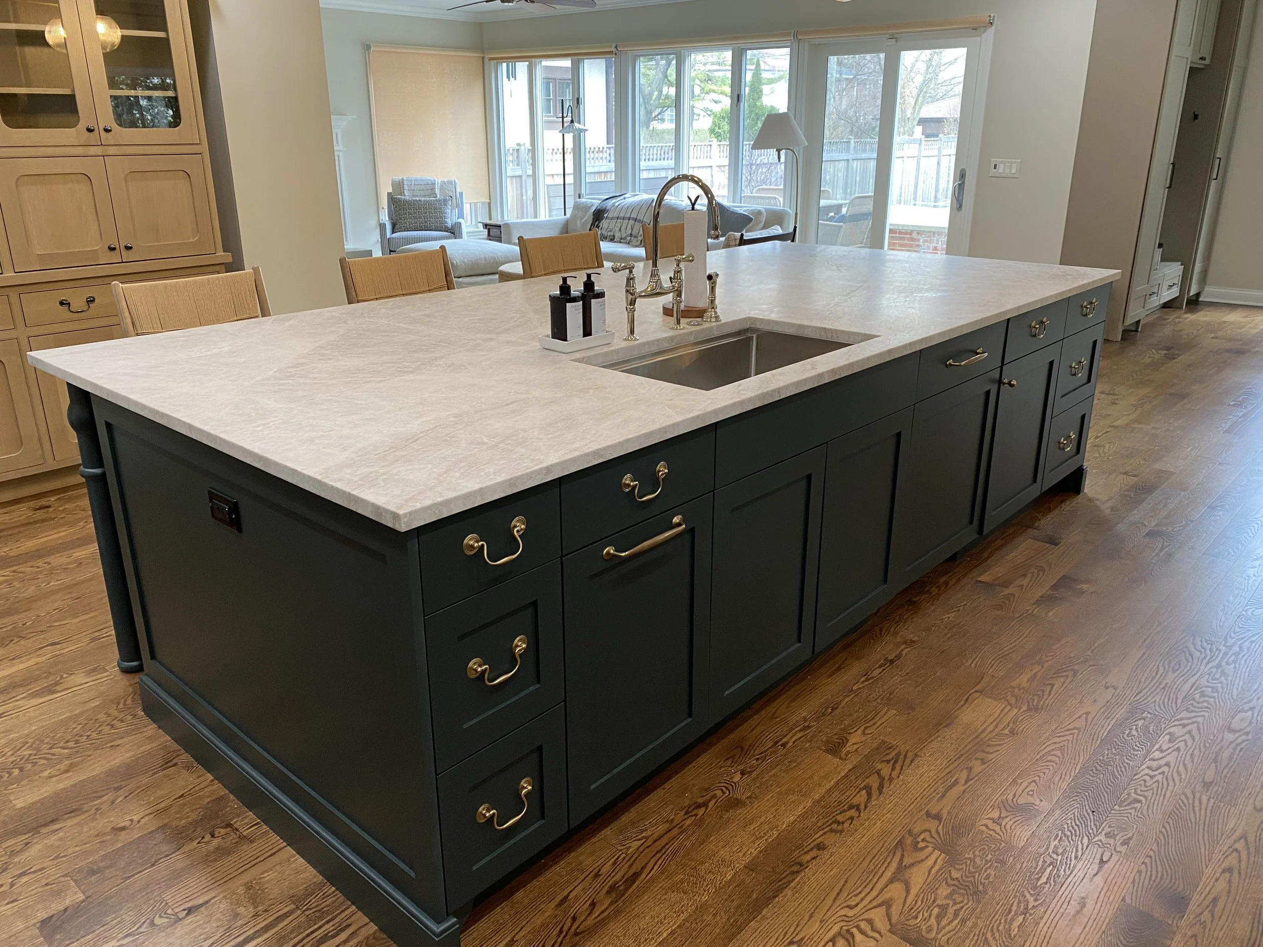 Kitchen island with a marble countertop, black cabinetry with gold handles, a sink, and a gold faucet, in a modern open-concept kitchen and living area.