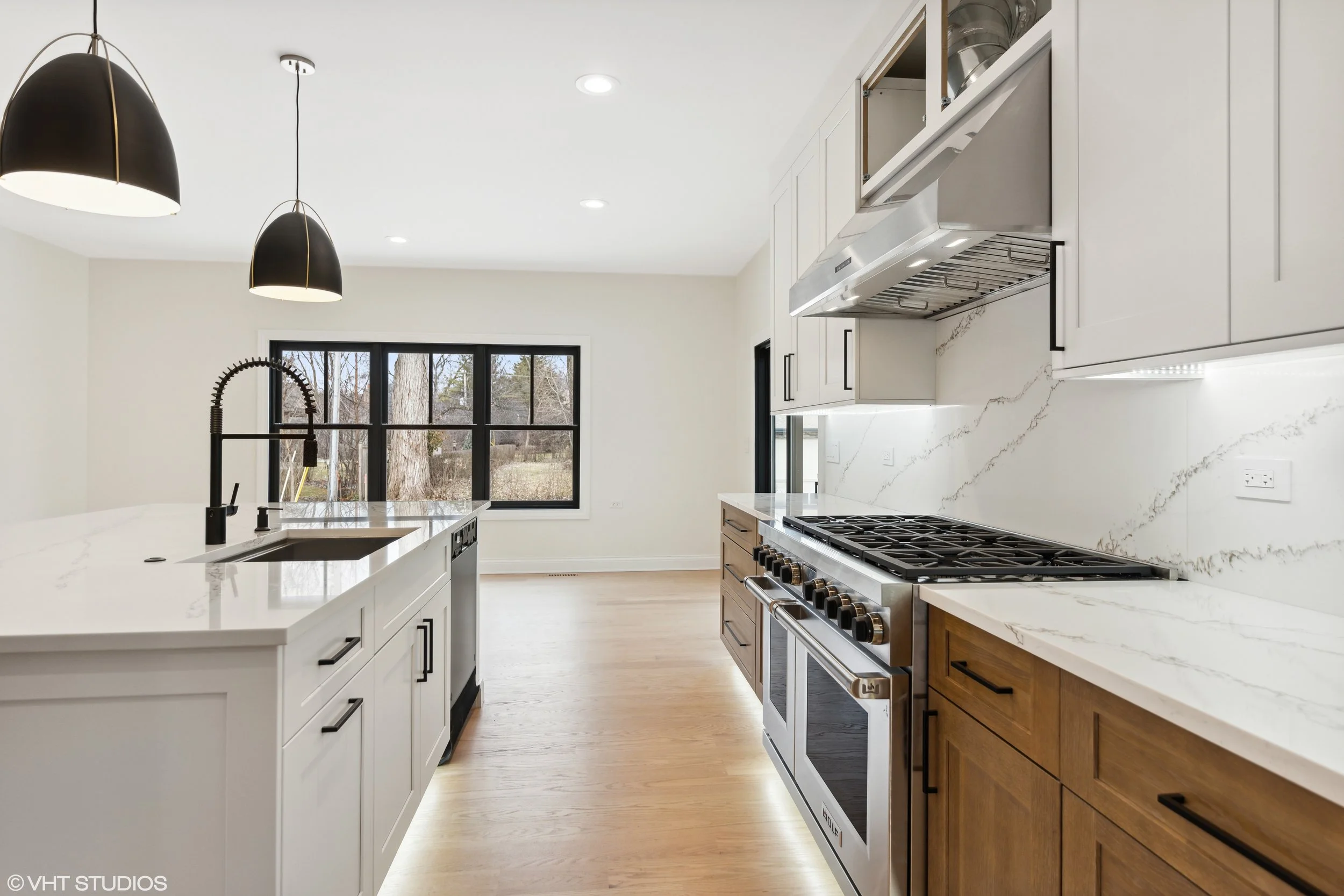 Modern kitchen with white cabinets, a marble backsplash, stainless steel appliances, a black sink with a high-arch black faucet, and large windows showing an outdoor view.
