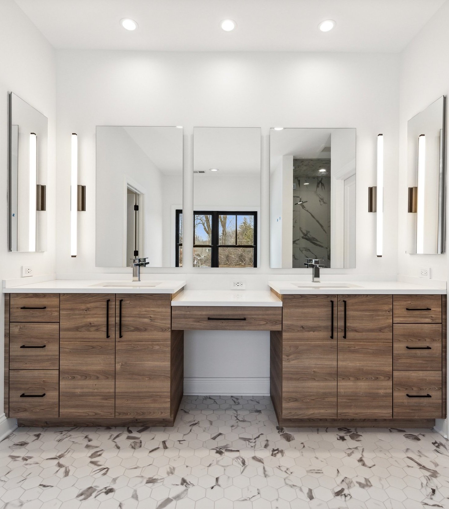 Modern bathroom vanity with two sinks, large mirror, white countertops, wooden cabinets, and hexagonal marble floor tiles.