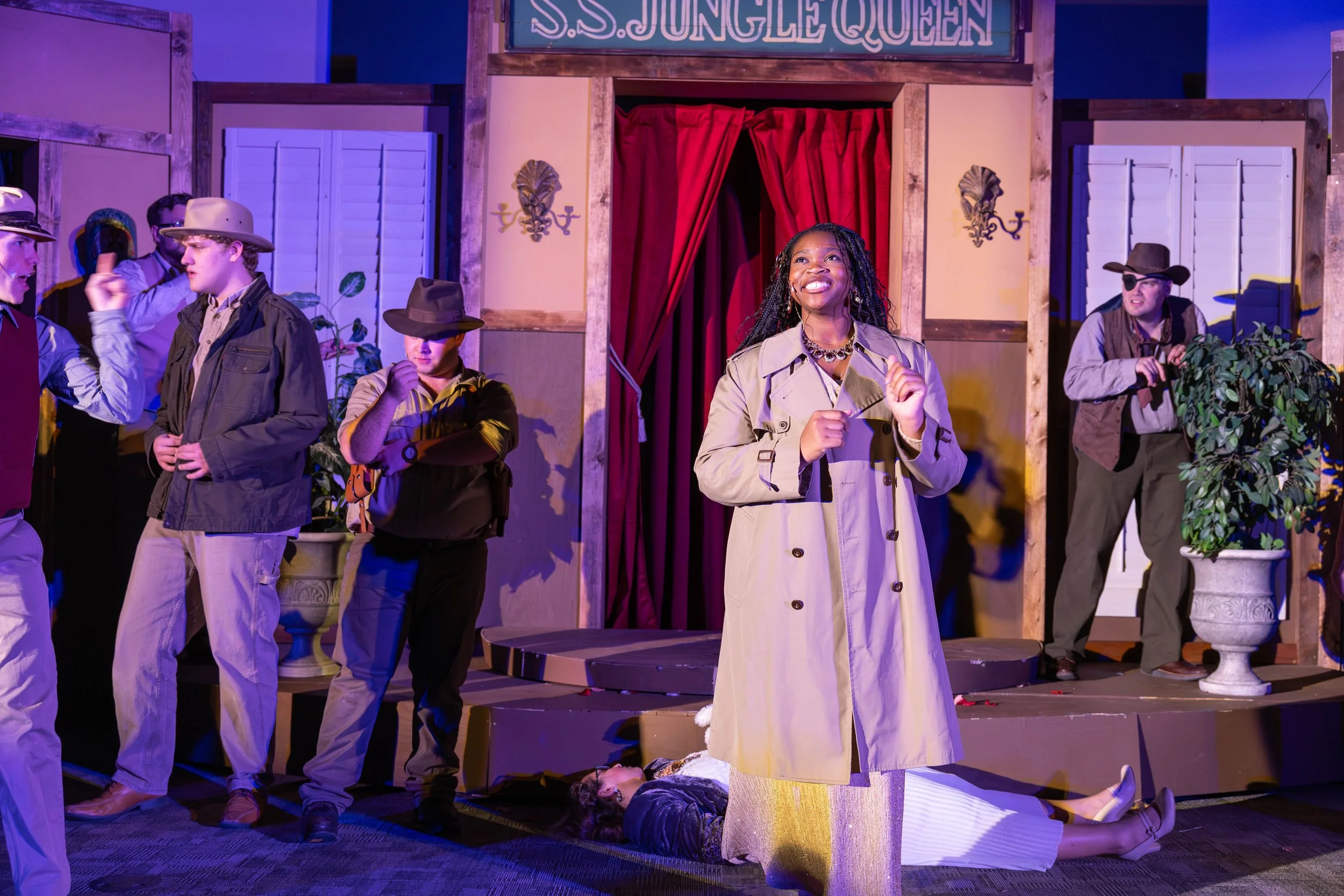 A stage production scene with several actors performing under stage lights, while a man in an eye patch and brown hat lurks suspiciously behind a potted plant in the background.