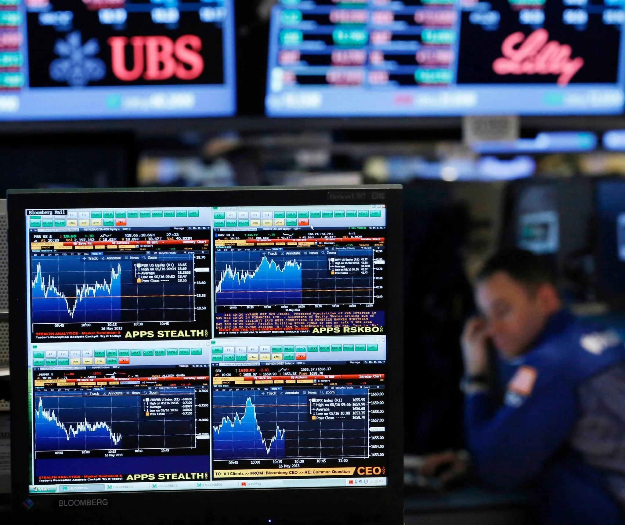 A financial trader looking at multiple computer screens displaying stock and market data at a trading floor.