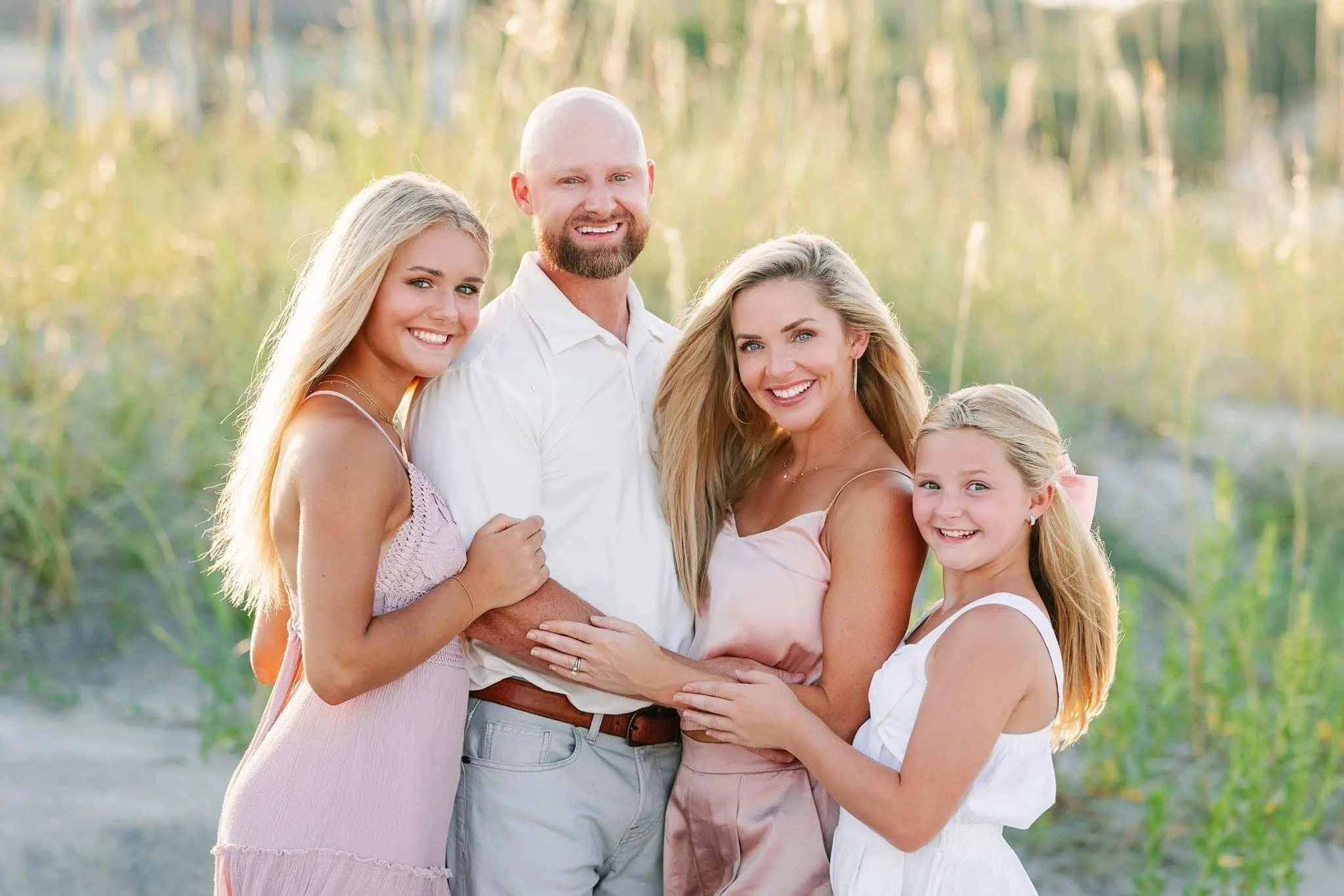 A happy family of five standing outdoors in a grassy field during sunset, smiling at the camera.