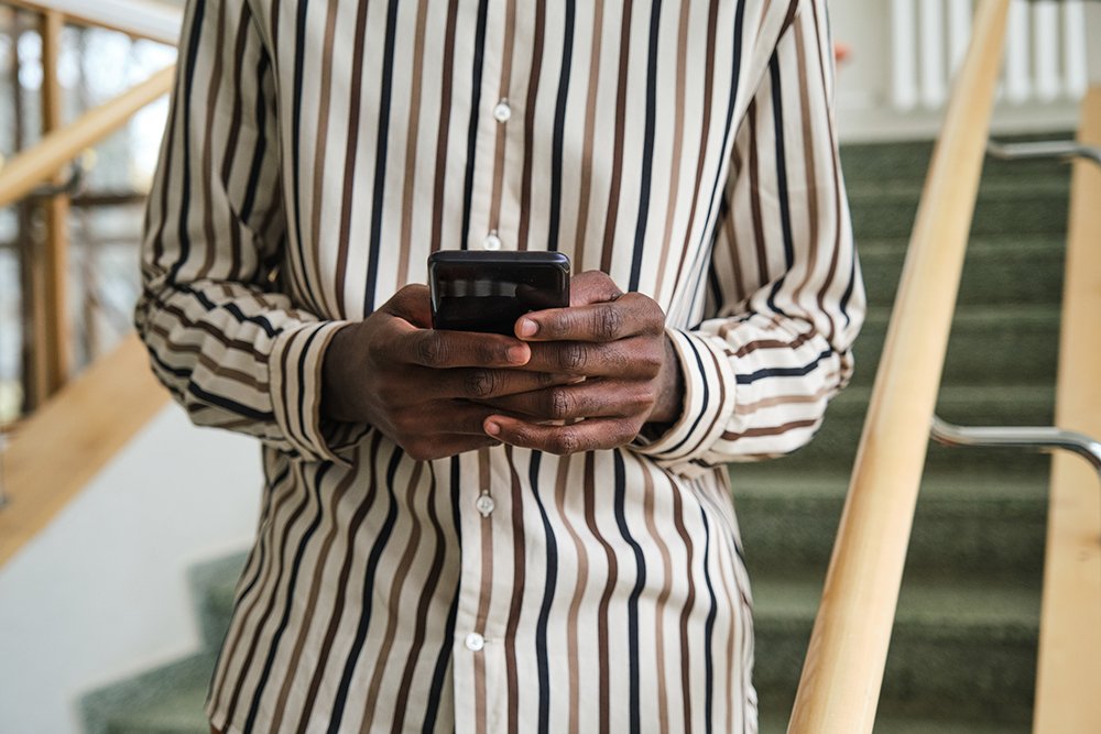 Person wearing a striped shirt using a smartphone on a staircase.